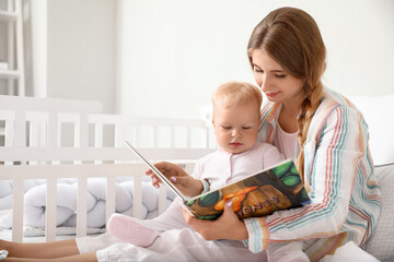 Young mother reading book to her cute little baby on bed