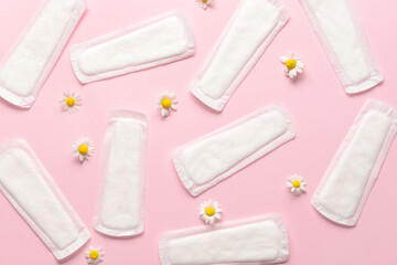 Menstrual pads and chamomile flowers on pink background