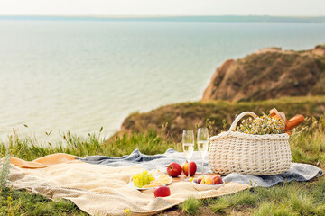 Wicker basket with tasty food and drink for romantic picnic in mountains near sea