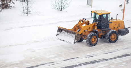 Big yellow tractor cleans up snow from the road and loads it into the truck. Cleaning and cleaning...