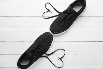 Pair of sportive shoes and hearts made of laces on light wooden background