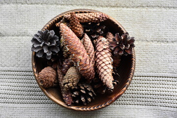 Wooden bowl filled with fir and pine cones on white knitted warm fabric. Home winter still-life