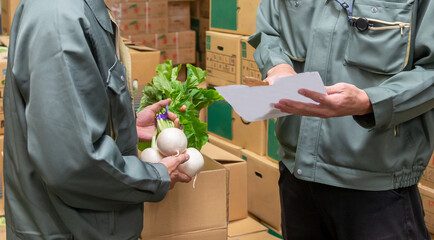 青果市場の倉庫で野菜を手に打ち合わせをする、作業着姿の2人の男性