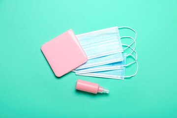 Medical masks with case and sanitizer on color background