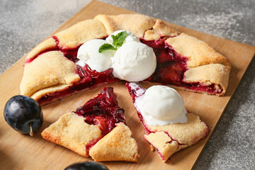 Board with cut tasty plum galette and ice cream on grunge background, closeup