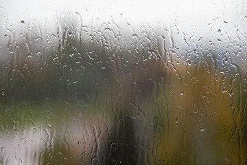 Rainy day through the window on cloudy grey sky and city buildings background. Concept. Evening cityscape behind the glass window with trickling drops of water.