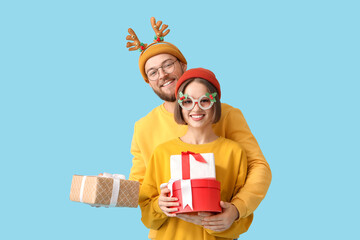 Happy young couple in stylish winter clothes and with Christmas gifts on color background