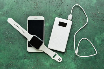 Modern power bank, smartwatch and mobile phone on green background