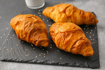 Board with delicious croissants on grunge background