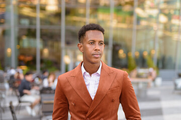 Portrait of handsome black African businessman outdoors in city thinking