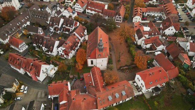 Church with red tile roof in middle of suburb community, Europe. Dietzenbach, Germany. Cinematic aerial pullback