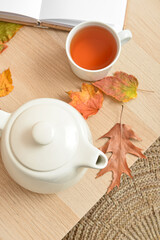 Tea pot, cup of hot beverage and autumn leaves on wooden background