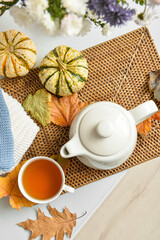 Tea pot, cup of hot beverage, pumpkins and autumn leaves on table in room