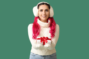 Beautiful woman in earmuffs with Christmas gift on green background