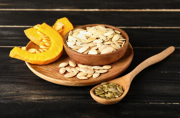 Bowl and spoon with natural pumpkin seeds on black wooden background