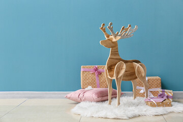Wooden reindeer with Christmas gifts and pillow near blue wall