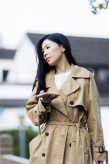 Stylish young asian woman dressed in casual wear looking away when posting photos in social media and thinking about interesting content text. Lifestyle blogger checking blog comments outdoor at