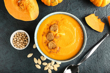 Bowl with delicious pumpkin cream soup and seeds on dark background