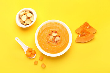 Bowl with delicious pumpkin cream soup and croutons on yellow background