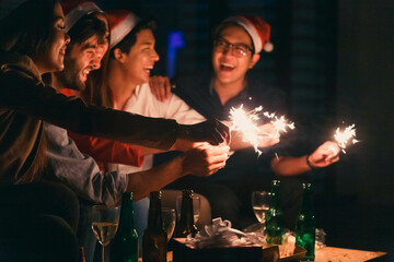 Happy multiracial people in party holding sparklers and champagne glasses celebrating New year eve together, excited diverse young friends having fun enjoying celebration together