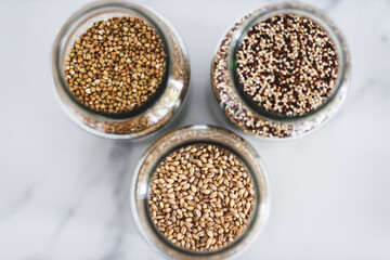 healthy whole grains and legumes in clear pantry jars on marble background including quinoa buckwheat and barley,, simple ingredients concept