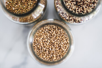 healthy whole grains and legumes in clear pantry jars on marble background including quinoa buckwheat and barley,, simple ingredients concept