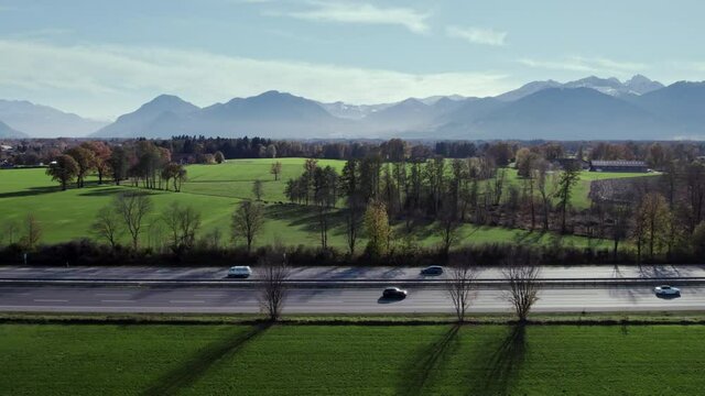Aerial Drone Shot of a Highway in southern Germany, Bavaria flying next to the smooth running traffic with multiple cars driving quite fast and overtake and the mountains in the background.