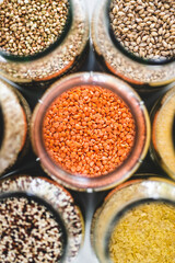 red lentils and other healthy whole grains and legumes in clear pantry jars on marble background, simple ingredients concept