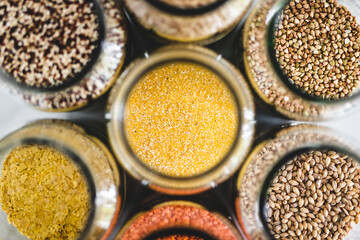 polenta cornmeal and other healthy whole grains and legumes in clear pantry jars on marble background, simple ingredients concept