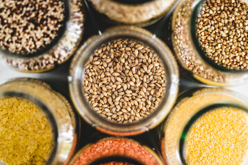 barley and other healthy whole grains and legumes in clear pantry jars on marble background, simple ingredients concept