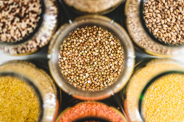 buckwheat and other healthy whole grains and legumes in clear pantry jars on marble background, simple ingredients concept