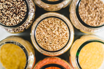 brown rice and other healthy whole grains and legumes in clear pantry jars on marble background, simple ingredients concept