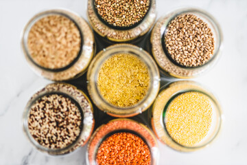 nutritional yeast and other healthy whole grains and legumes in clear pantry jars on marble background, simple ingredients concept
