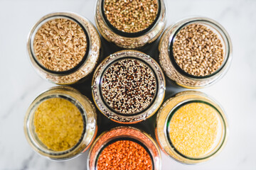 quinoa and other healthy whole grains and legumes in clear pantry jars on marble background, simple ingredients concept