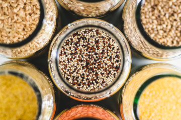 quinoa and other healthy whole grains and legumes in clear pantry jars on marble background, simple ingredients concept