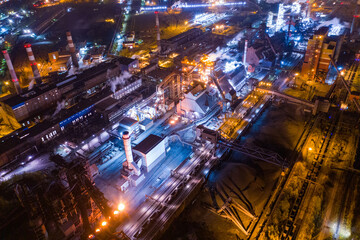 Fototapeta na wymiar Aerial view of steel plant at night with smokestacks and fire blazing out of the pipe. Industrial panoramic landmark with blast furnance of metallurgical production. Concept of environmental pollution