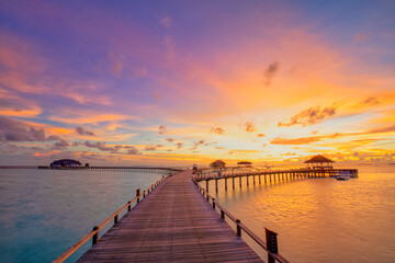 Sunset on Maldives island, luxury water villas resort hotel and wooden pier. Colorful sky and...