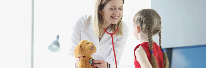 Pediatrician shows little girl how to use stethoscope using toy as example