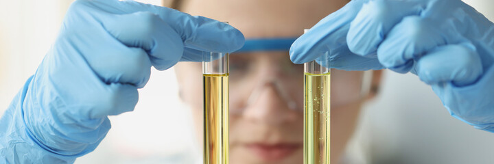 Woman chemist holds in hands two test tubes with yellow transparent liquid for research