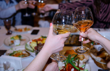 Toast at the festive table. Woman's hands holding glasses with alcoholic beverages, close-up. Friends clinking wineglasses.