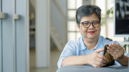 Cheerful mature female using smartphone at home
