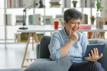 Gleeful Asian female using tablet at home