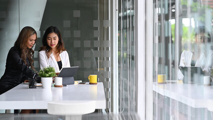 Two young businesswomen analyzing business at a on computer tablet together.