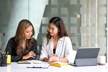 Two businesswomen sitting at office desk and talking about project startup ideas.