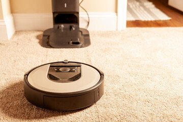 Close up generic image for robot vacuum cleaner. This unit is operating on carpetted floor and heading towards its base station for charging and emptying its bag. A convenient home automation - obrazy, fototapety, plakaty