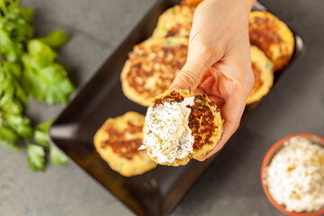 Turkish style zucchini pancakes or fritters known as mucver, served on black plate with fresh greens and sour cream. Close up  top view image with a woman holding a piece in hand.