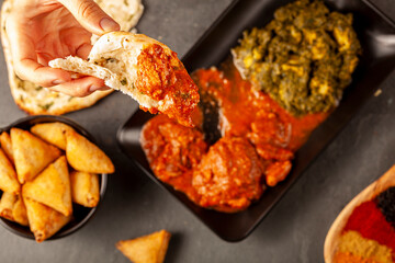 A woman is eating delicious Indian food with various dishes. She dips naan bread into curry. Concept for eating asian cuisine or restaurant with a variety of selections.