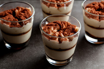 Delicious traditional tiramisu dessert served in small glass cups on stone countertop. Low light image shows texture and layers from angle with shallow depth of field. - obrazy, fototapety, plakaty