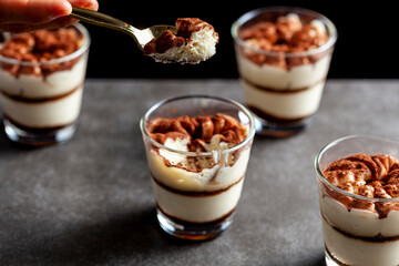 Delicious traditional tiramisu dessert served in small glass cups on stone countertop. Low light image shows texture and layers from angle with shallow depth of field.