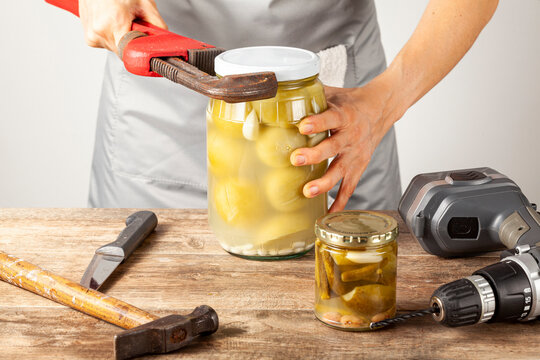 A funny quirky concept image showing a caucasian woman trying to open a jar of pickles. She is trying with tools like drill, knife, wrench and hammer